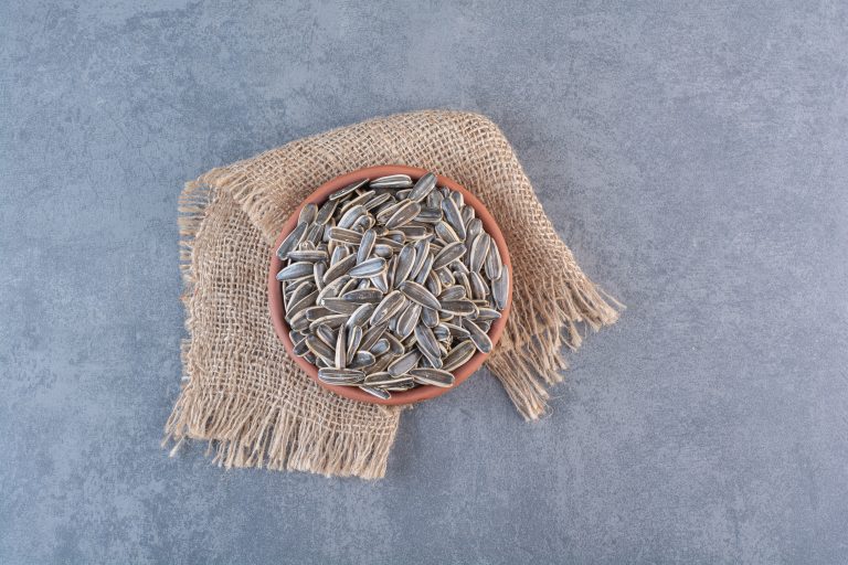 Unpeeled sunflower seeds in clay plate on texture , on the marble background